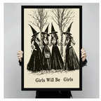 Close-up of a gothic art print being held up, depicting four witches in Victorian-style black dresses and pointed hats in a woodland scene, with Girls Will Be Girls printed in bold serif font at the bottom