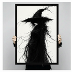 Person holding a large black framed gothic witch art print featuring a mysterious dark figure with branch-like flowing hair and a pointed hat, shown against a neutral gray background